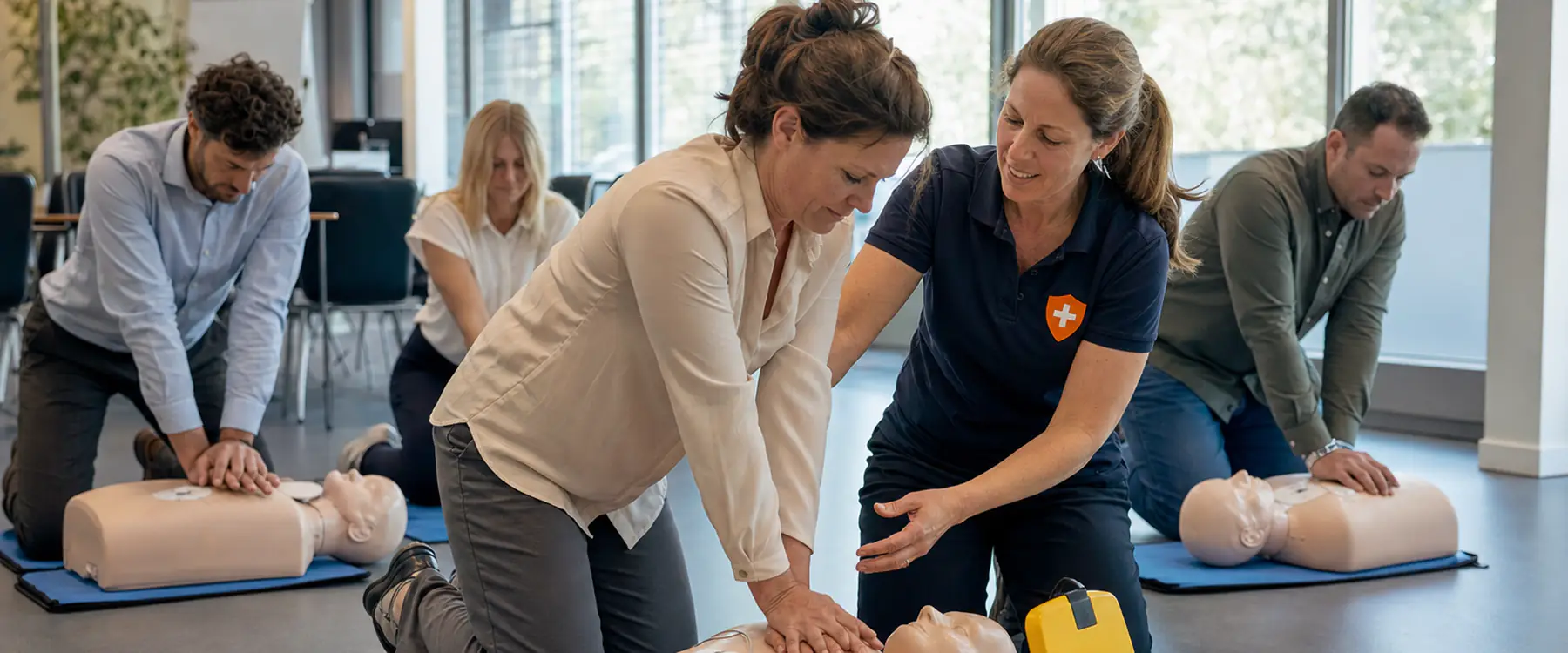 Cursisten oefenen reanimatie op oefenpoppen met een AED-trainer, de instructeur corrigeert de handpositie