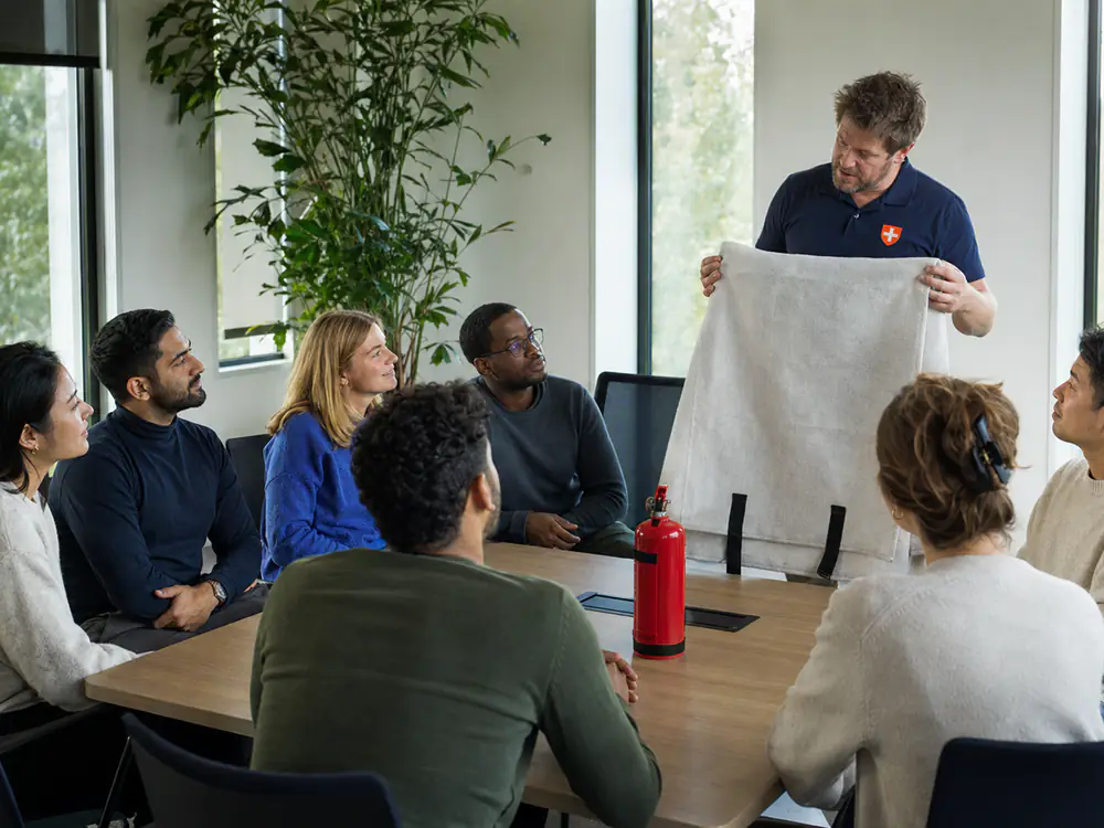 Internationaal team volgt een BHV-training in het Engels, de instructeur toont een blusdeken
